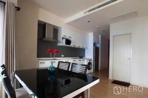 คอนโด ให้เช่าหรือขายในWatthana, Bangkok - พื้นที่รับประทานอาหาร โต๊ะสีดำเงาเก้าอี้สี่ตัว ติดกับครัวบิวท์อินในแปลนเปิด