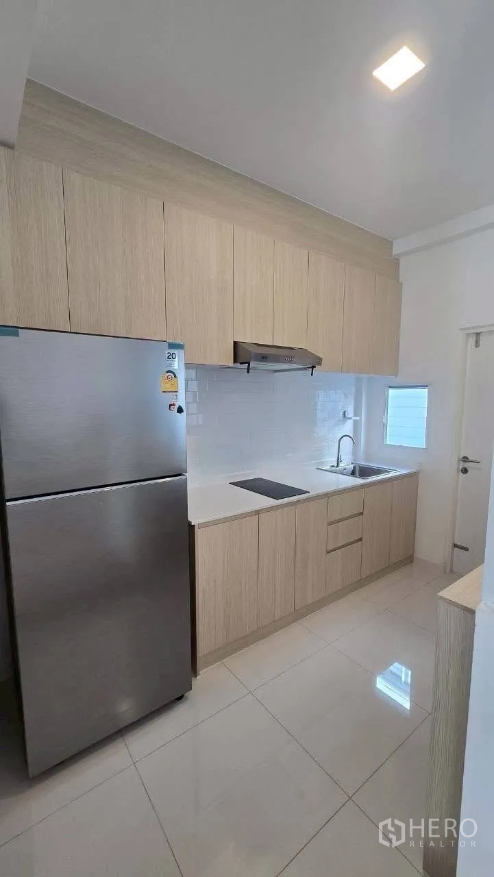 Townhouse for rent in Prawet, Bangkok - Sleek light-wood kitchen with cabinets, cooktop, hood, sink and stainless fridge.