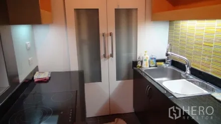 Condominium for rent or sale in Sathon, Bangkok - Compact separate kitchen featuring black countertops, electric hob, sink, and a yellow tile backsplash.