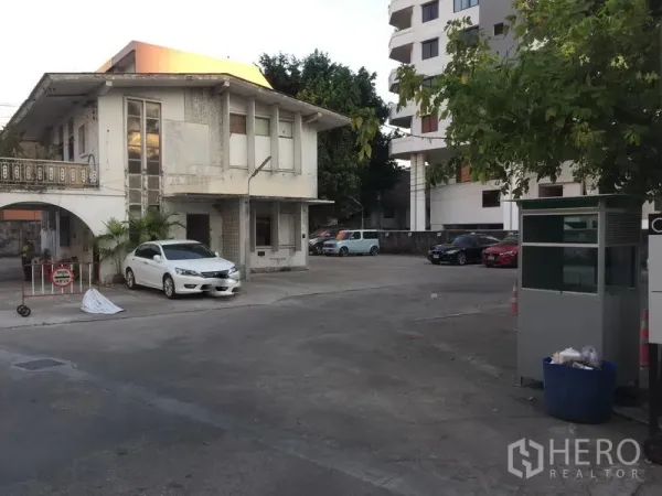 พื้นที่ขายปลีก ให้เช่าในKhlong Toei, Bangkok - อาคารสองชั้นมีซุ้มโค้งและป้อมยาม ข้างลานจอดรถคอนกรีตกว้าง ย่านทองหล่อ