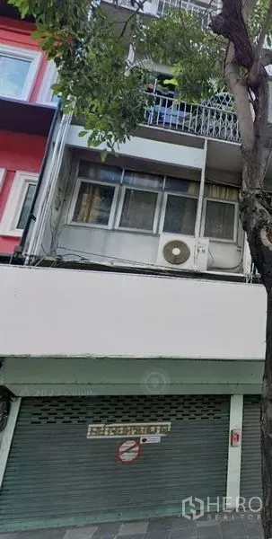 อาคารพาณิชย์ ให้เช่าในKhlong Toei, Bangkok - ด้านหน้าอาคารพาณิชย์หลายชั้น ประตูม้วนสีเขียว มีระเบียงและต้นไม้ริมถนน ในย่านสุขุมวิท