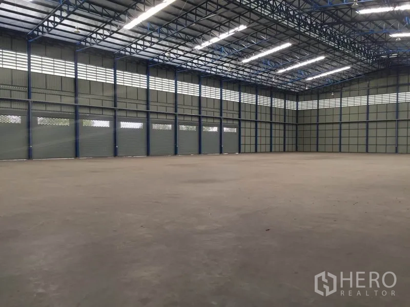 Warehouse for rent in Pak Kret, Nonthaburi - Open warehouse hall showing multiple roller shutter doors and ventilated wall panels.