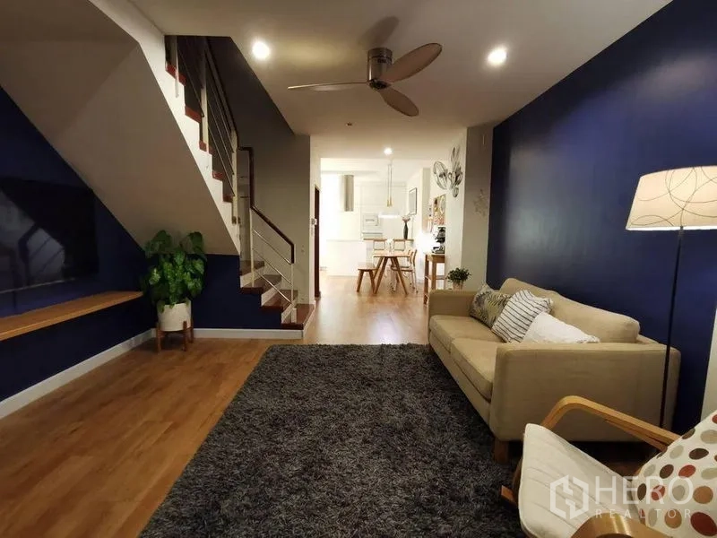 ทาวน์เฮาส์ ให้เช่าหรือขายในYan Nawa, Bangkok - ห้องนั่งเล่นแบบโอเพนแพลน ผนังสีน้ำเงิน บันได โซฟา พัดลมเพดาน พรม และทีวีติดผนัง