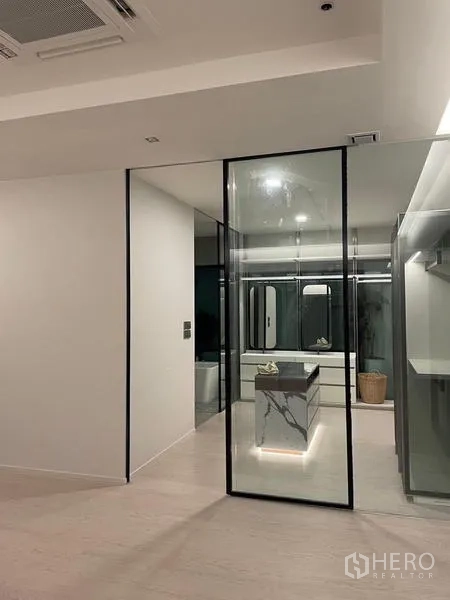 Detached House for rent or sale in Saphan Sung, Bangkok - Dressing room at night with illuminated marble island, mirrors and glass door.