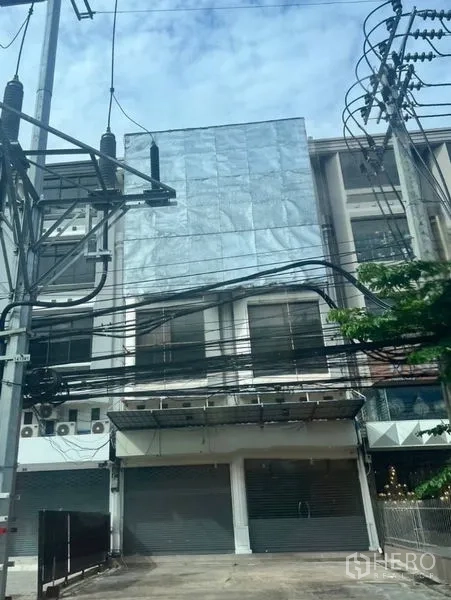 Shophouse for rent in Khan Na Yao, Bangkok - Street-facing multi-storey shophouse exterior with closed roller shutters, wide frontage, metal-clad facade and balconies in Khan Na Yao, Bangkok.