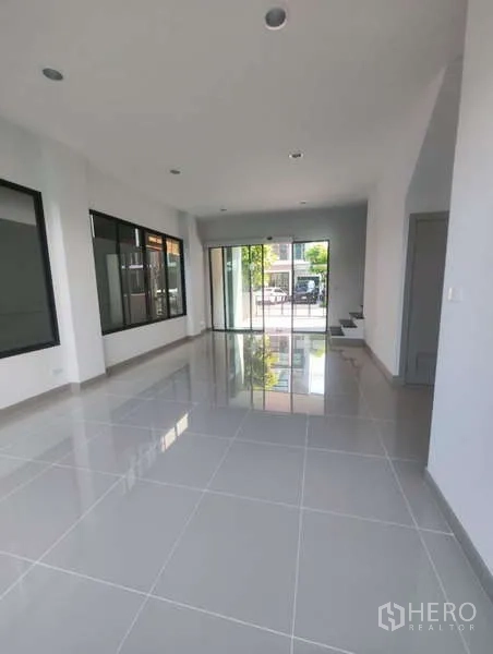 Home Office for rent in Bueng Kum, Bangkok - Open-plan ground floor workspace with big windows, reflective tiles, and sliding doors leading to the front parking area.