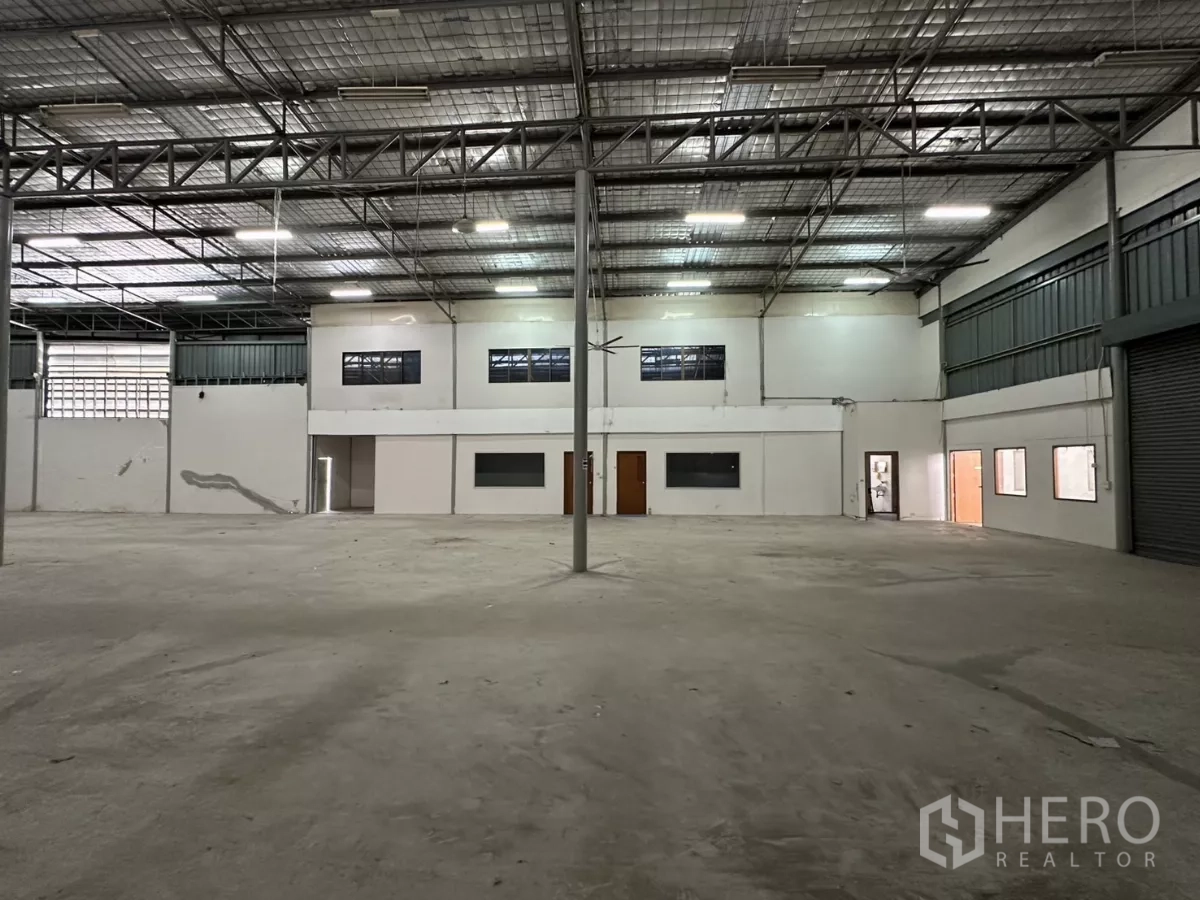 Warehouse for rent in Suan Luang, Bangkok - Warehouse view facing the office section with windows, roller shutter, and bright overhead lighting.