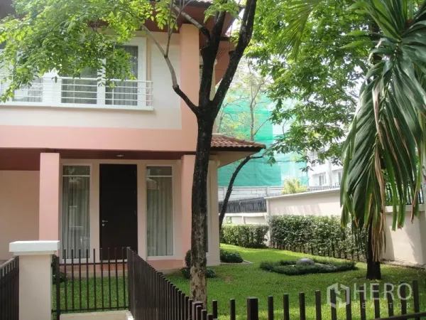 Detached House for rent in Wang Thonglang, Bangkok - Corner view of the house with large windows, metal fence and landscaped yard.