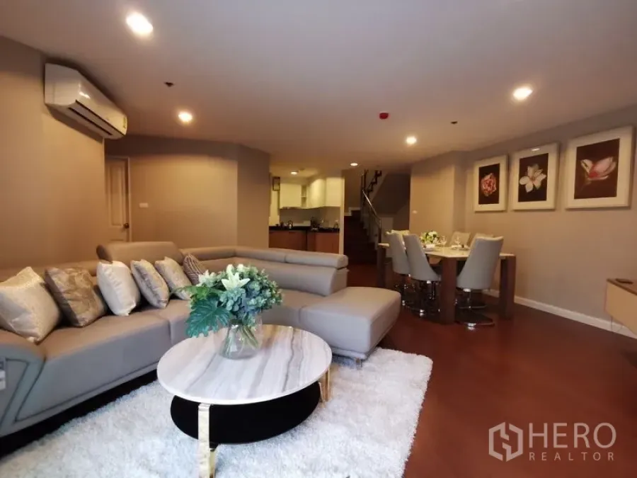 Condominium for rent or sale in Huai Khwang, Bangkok - Large living–dining area with sectional sofa, marble coffee table, and view to kitchen and stairs.