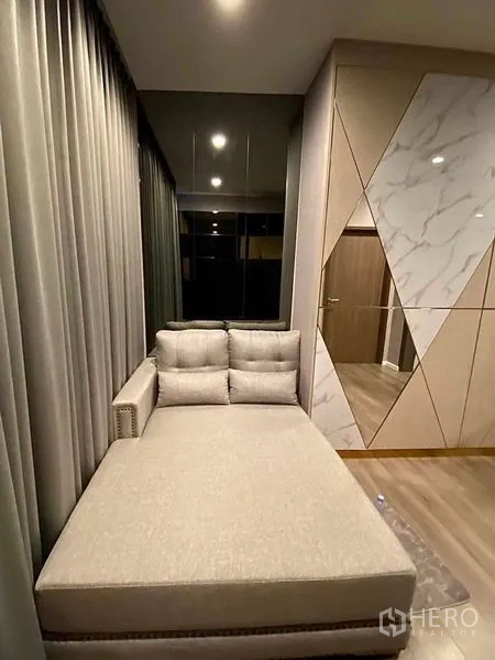Condominium for rent in Phra Khanong, Bangkok - Daybed lounge beside floor-to-ceiling curtains and geometric marble-pattern wall panels.