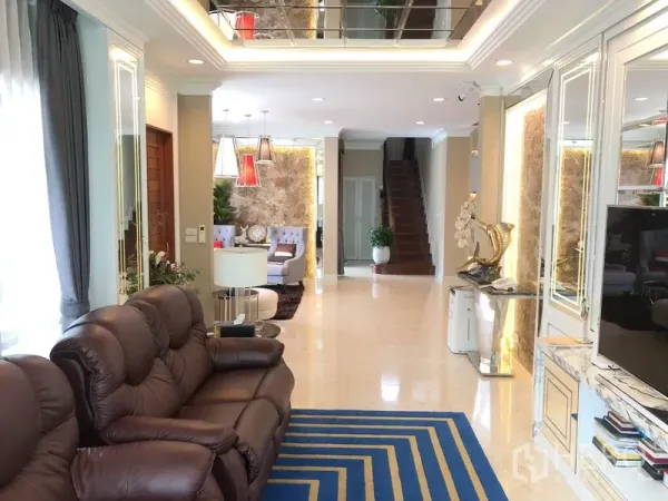 Detached House for rent or sale in Saphan Sung, Bangkok - Open-plan lounge with leather sofa, recessed lighting, and a staircase to the upper floors.