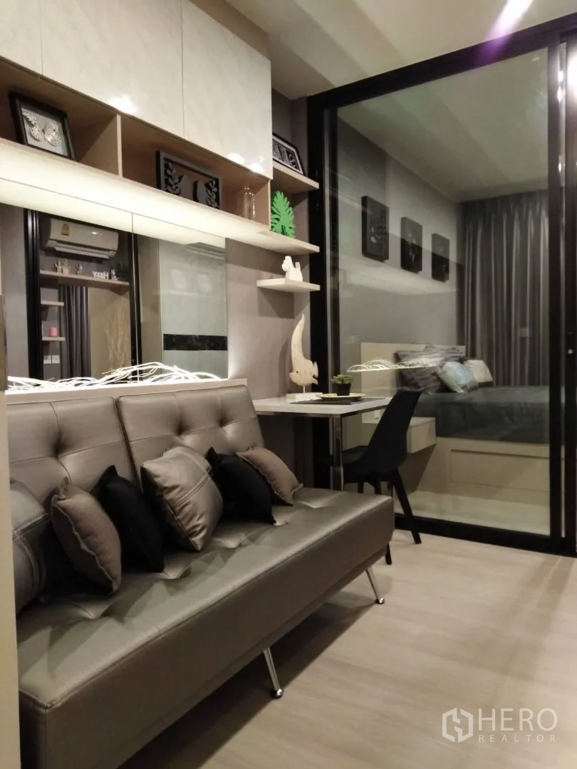 Condominium for rent in Huai Khwang, Bangkok - Cozy living area with grey sofa, wall shelves and study desk facing the bedroom