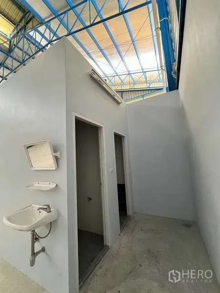 Warehouse for rent in Lat Lum Kaeo, Pathum Thani - Interior service area with sink and doors beneath a high steel roof.