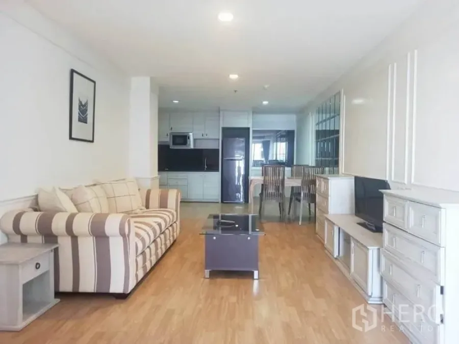 公寓 出租在Khlong Toei, Bangkok - 明亮的开放式客厅，条纹沙发、电视柜与一体化厨房。