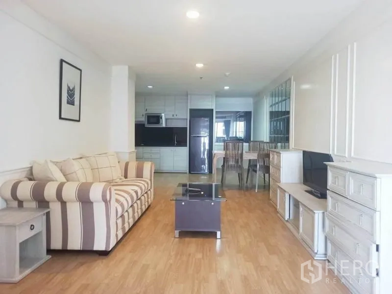 公寓 出租在Khlong Toei, Bangkok - 明亮的开放式客厅，条纹沙发、电视柜与一体化厨房。