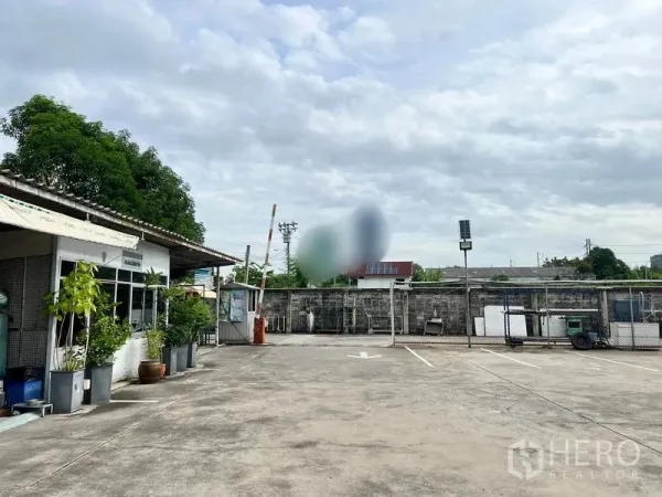 ที่ดิน ให้เช่าในBang Na, Bangkok - ออฟฟิศชั้นเดียวหน้าต่างบานเลื่อน พร้อมกระถางต้นไม้ ข้างลานคอนกรีตและจุดเข้าออกที่มีรั้ว