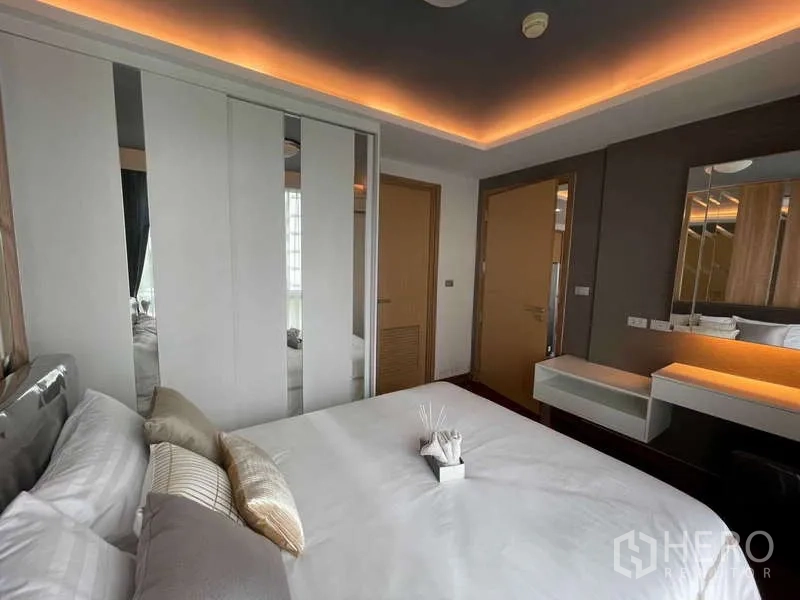 คอนโด ขายในWatthana, Bangkok - ห้องนอนหลักเพดานซ่อนไฟ ตู้เสื้อผ้าบานเลื่อน และโต๊ะเครื่องแป้ง โทนสีอบอุ่น