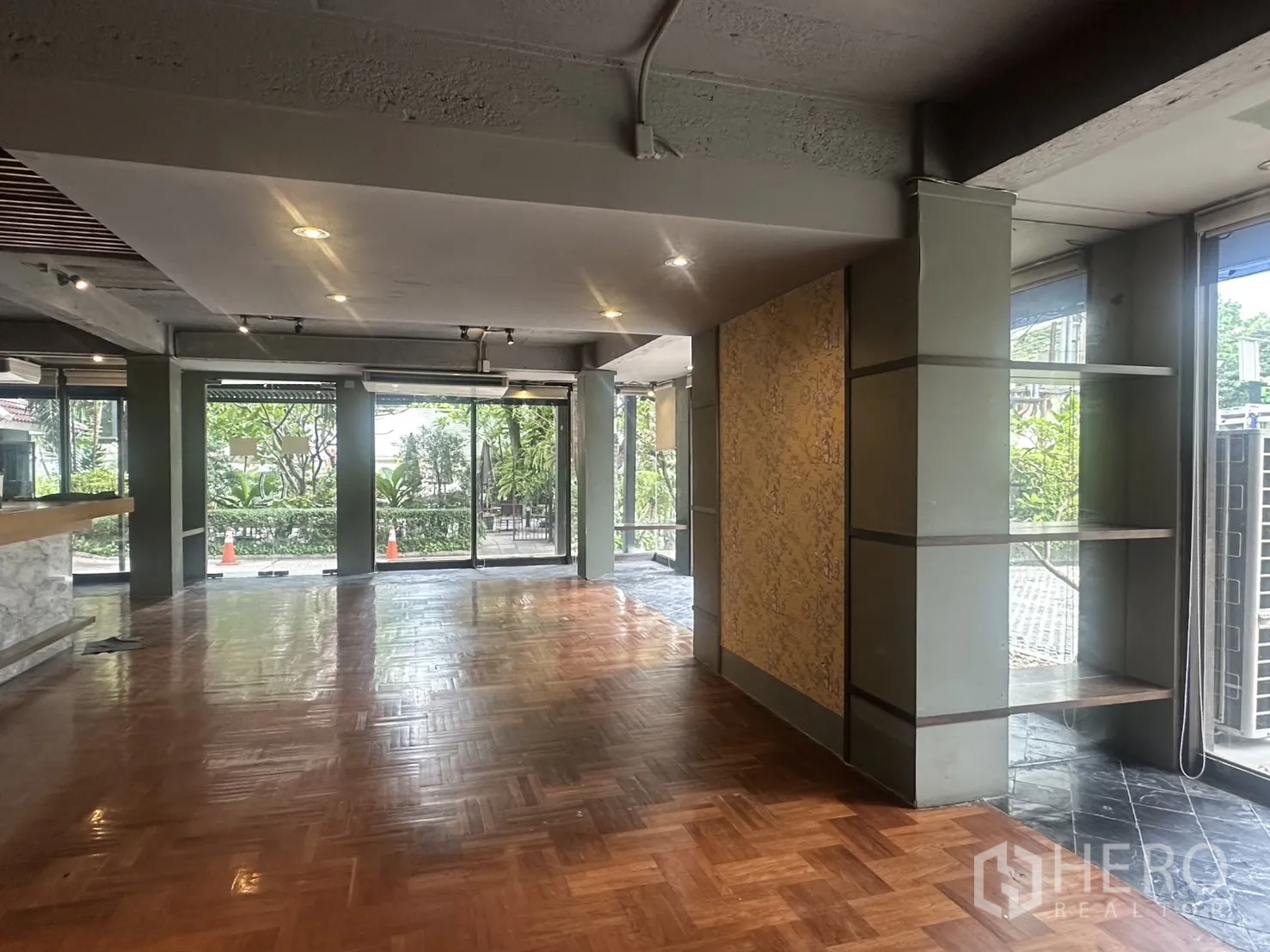Retail Space for rent in Watthana, Bangkok - Spacious shop floor with built-in bar counter, display shelving, and floor-to-ceiling windows facing greenery.