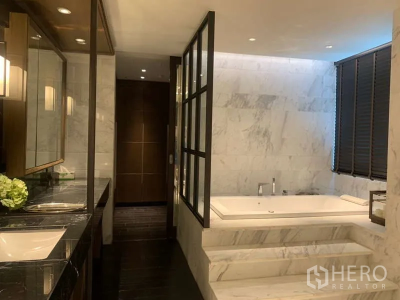 Condominium for rent in Khlong Toei, Bangkok - Spa-like bathroom featuring a raised marble soaking tub with steps beside a shuttered window.