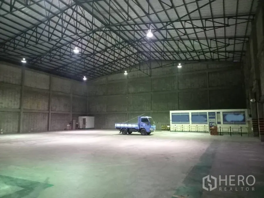 Warehouse for rent in Mueang Pathum Thani, Pathum Thani - Spacious warehouse interior with steel truss roof, high ceiling, bright lighting and a truck on the concrete floor.