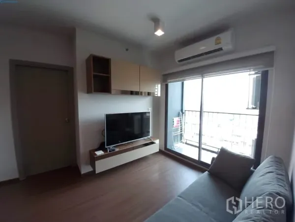 公寓 出租在Phra Khanong, Bangkok - 客厅设沙发与电视柜，推拉落地门通向阳台。