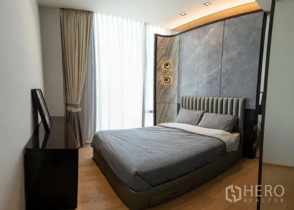 Condominium for rent - Bedroom with gray upholstered bed, curved stone feature wall and sheer curtains.