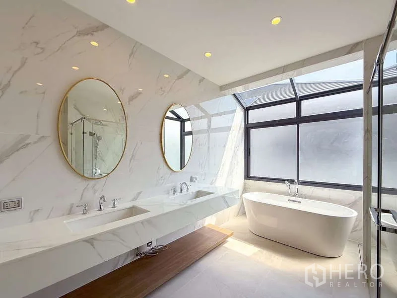 Detached House for rent or sale in Bang Kapi, Bangkok - Sunlit bathroom with double vanity, round mirrors and a freestanding bathtub.