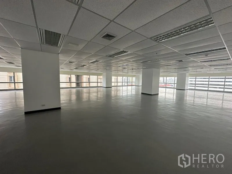 Office Space for rent - Spacious empty office interior with columns, drop ceiling, fluorescent lighting and wraparound windows.