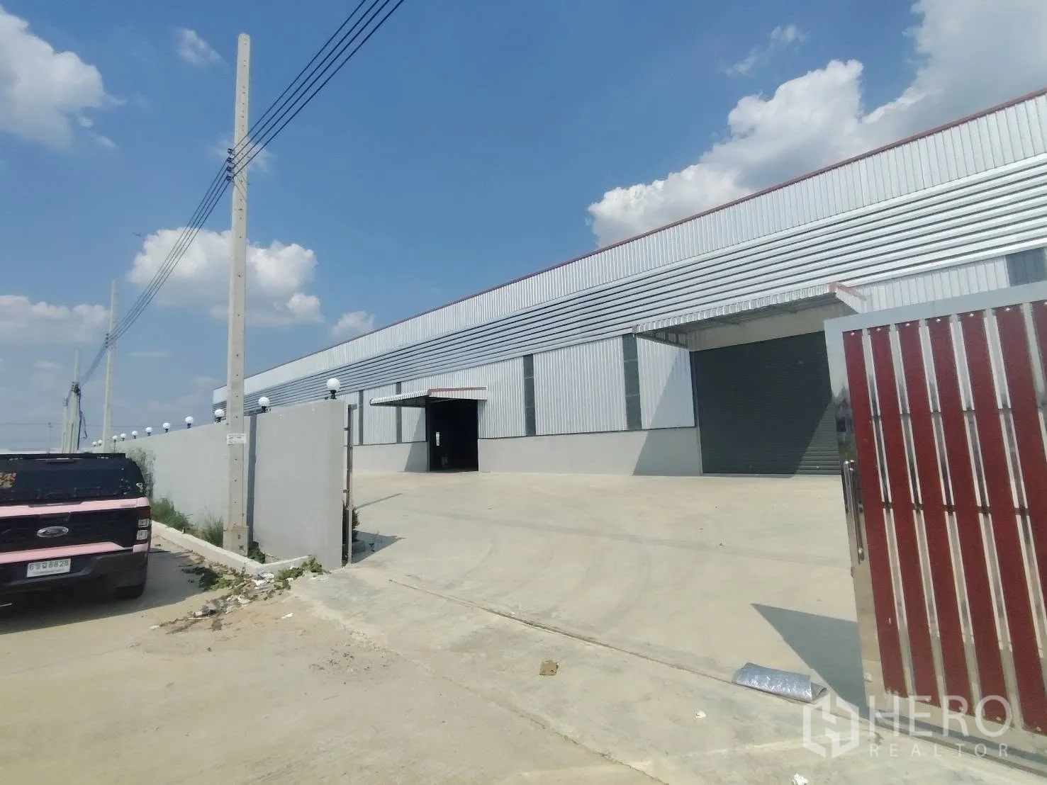 Warehouse for rent in Bang Phli, Samut Prakan - Entrance driveway and gate leading to the warehouse with large roller door and perimeter wall.