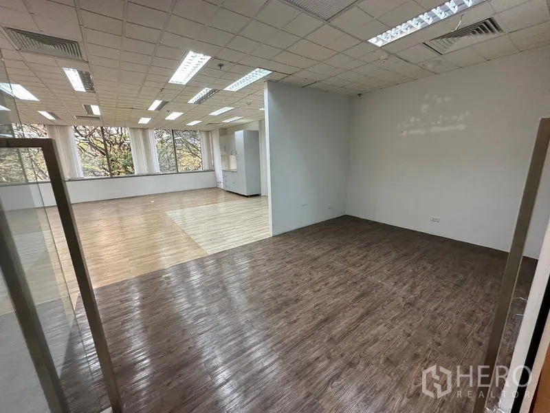 สำนักงาน ให้เช่า - ห้องกระจกพื้นไม้สีเข้ม เชื่อมต่อโถงสำนักงานขนาดใหญ่ เพดานไฟสว่างและวิวต้นไม้.