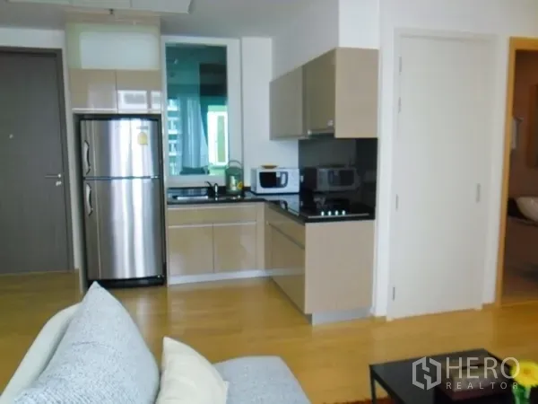 Condominium for rent or sale in Watthana, Bangkok - Modern compact kitchen with glossy cabinets, stainless refrigerator, cooktop and microwave in an open-plan layout.