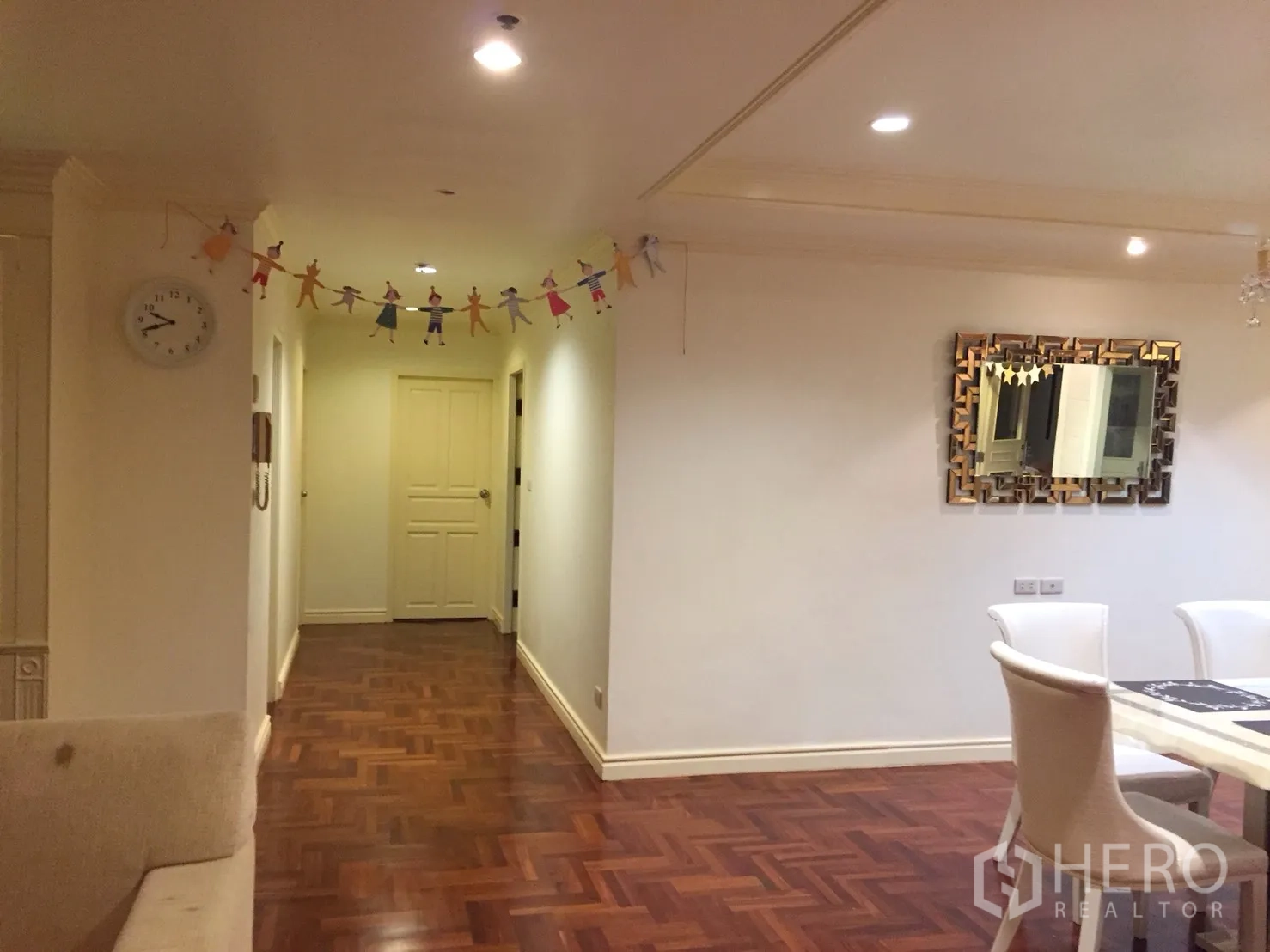 Condominium for rent in Watthana, Bangkok - Hallway leading to bedrooms with parquet flooring, recessed ceiling lights, and a decorative wall mirror.