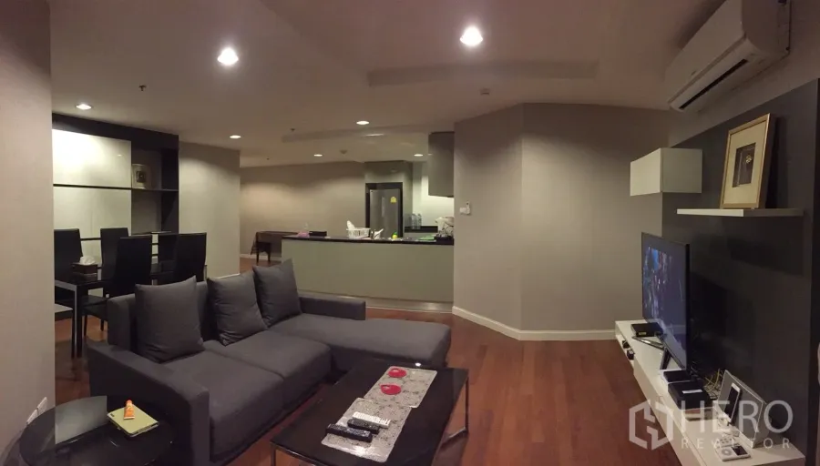 Condominium for rent in Huai Khwang, Bangkok - Open-plan living room with gray sofa, TV feature wall and warm wood flooring.