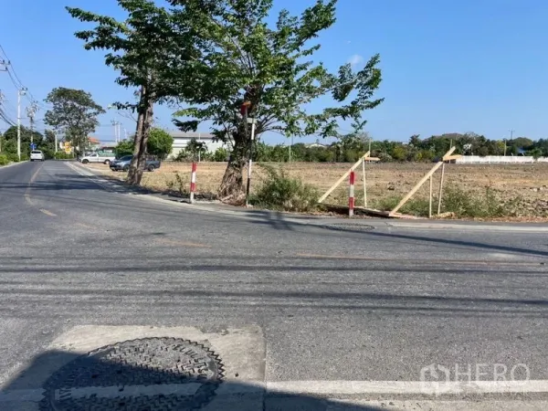 Land for sale in Mueang Samut Prakan, Samut Prakan - Access to a vacant land parcel along a two-lane road with trees and boundary stakes in Phraeksa