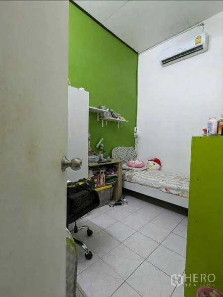 Shophouse for sale in Samphanthawong, Bangkok - Small air-conditioned bedroom with a green accent wall, shelving and tiled floor in Samphanthawong.