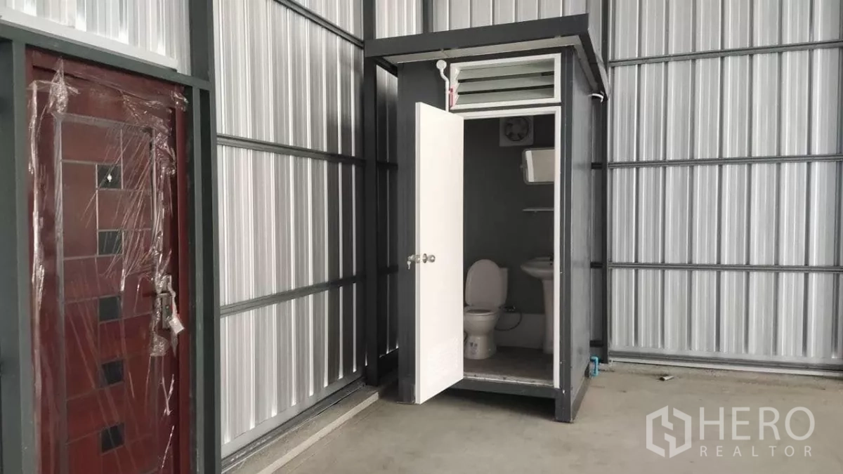 Warehouse for rent in Bang Lamung, Chon Buri - Built-in warehouse restroom with toilet and sink inside metal-panel structure.