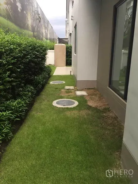 Detached House for sale in Pak Kret, Nonthaburi - Narrow side garden with trimmed hedge, grass lawn and utility covers