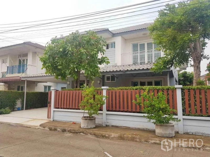 Detached House for sale in Nonthaburi - Two-storey detached house exterior with balcony and fenced front yard.