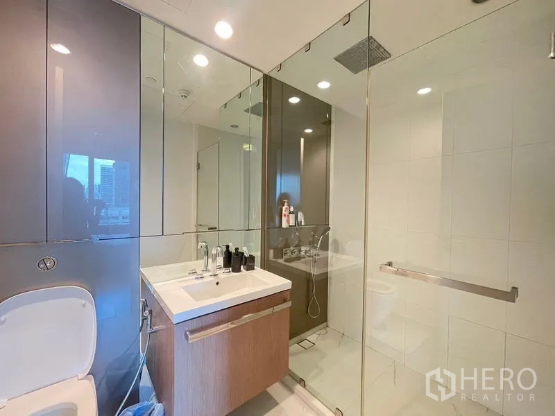 Condominium for rent in Pathum Wan, Bangkok - Second bathroom with glass shower, floating vanity and toilet.