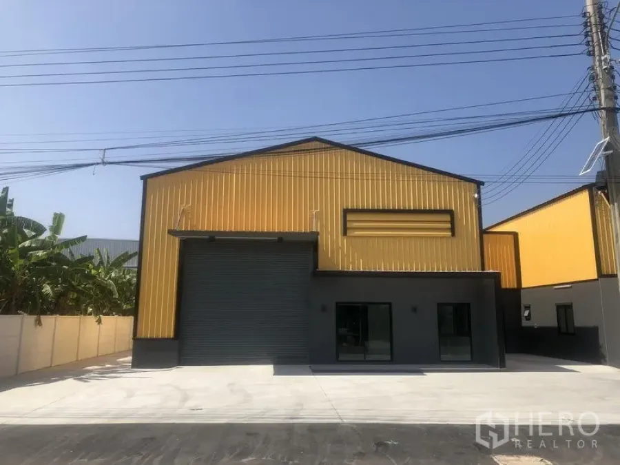 工厂 出租在Bang Yai, Nonthaburi - 单一厂房正面，高挑卷闸门与玻璃办公区，停车方便。