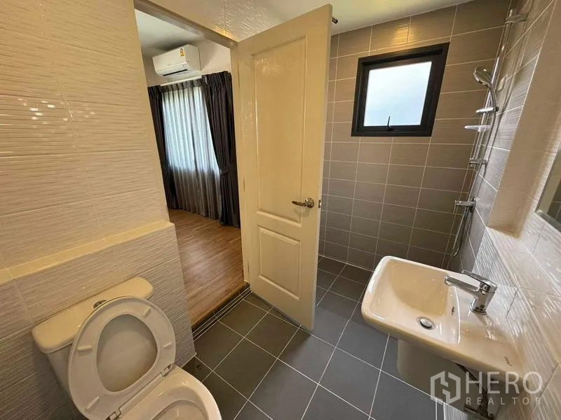 Detached House for rent in Don Mueang, Bangkok - Bathroom with gray tiles, shower area and window connecting to bedroom.