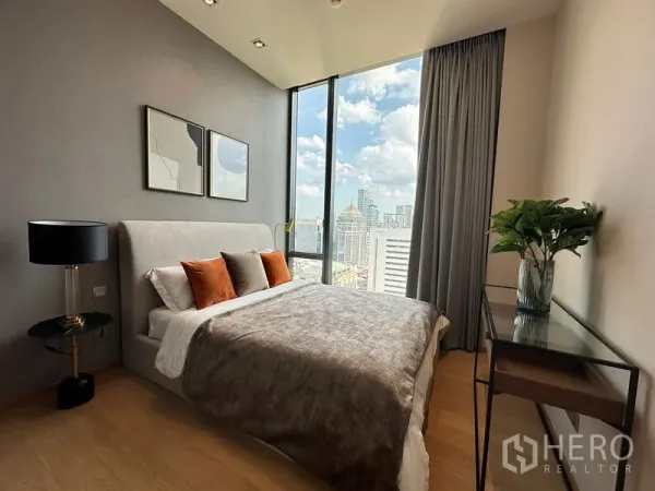 Condominium for rent in Pathum Wan, Bangkok - Bedroom with upholstered bed and skyline view from floor-to-ceiling windows.