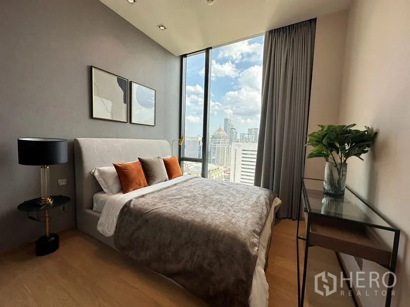 Condominium for rent in Pathum Wan, Bangkok - Bedroom with upholstered bed and skyline view from floor-to-ceiling windows.