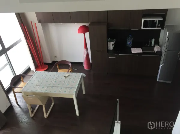 Condominium for rent in Ratchathewi, Bangkok - Compact kitchen with dark wood cabinets, microwave, fridge and a dining table beside large windows.