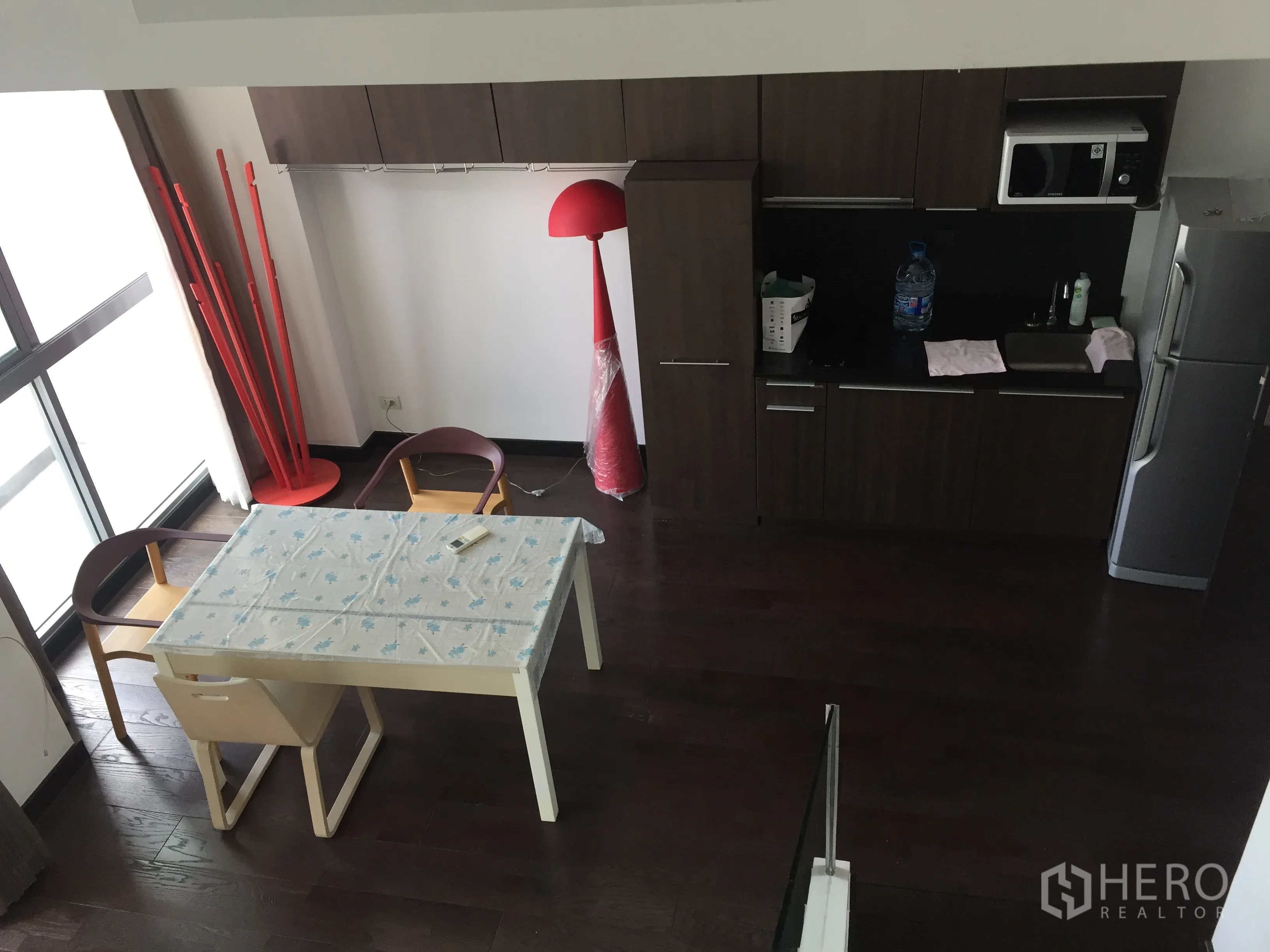 Condominium for rent in Ratchathewi, Bangkok - Compact kitchen with dark wood cabinets, microwave, fridge and a dining table beside large windows.