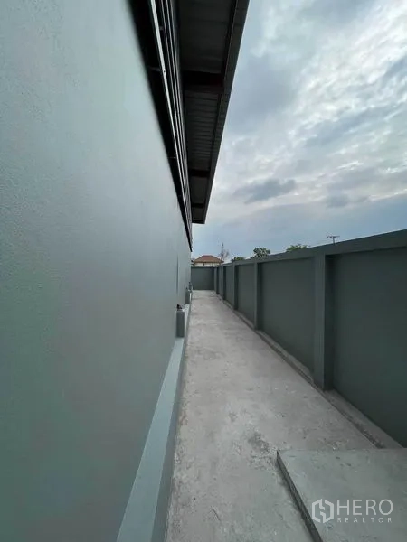 Warehouse for rent in Khlong Sam Wa, Bangkok - Narrow service walkway along the warehouse and boundary wall under a cloudy sky.