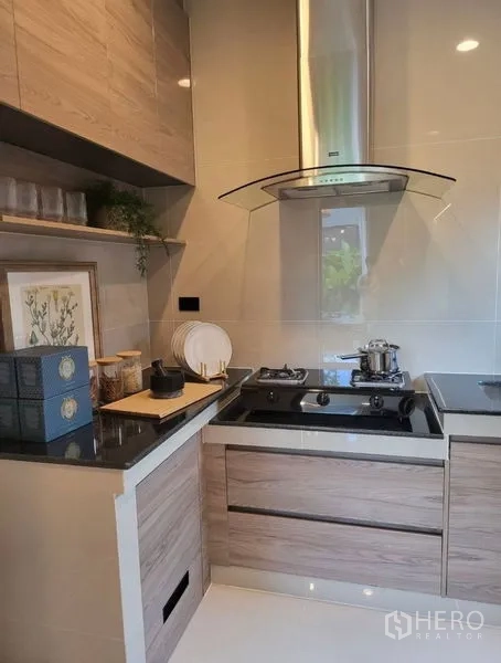 Detached House for rent in Bang Kapi, Bangkok - Modern compact kitchen with gas cooktop, stainless-steel hood and wood cabinetry.
