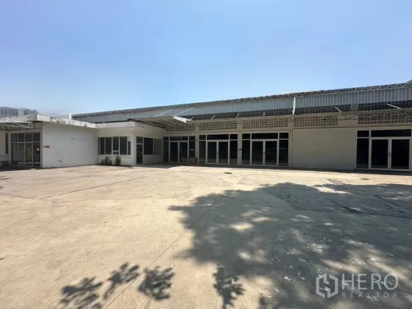 Warehouse for rent in Din Daeng, Bangkok - Single-story warehouse exterior with a wide concrete yard and glass-front entrances under a metal awning.