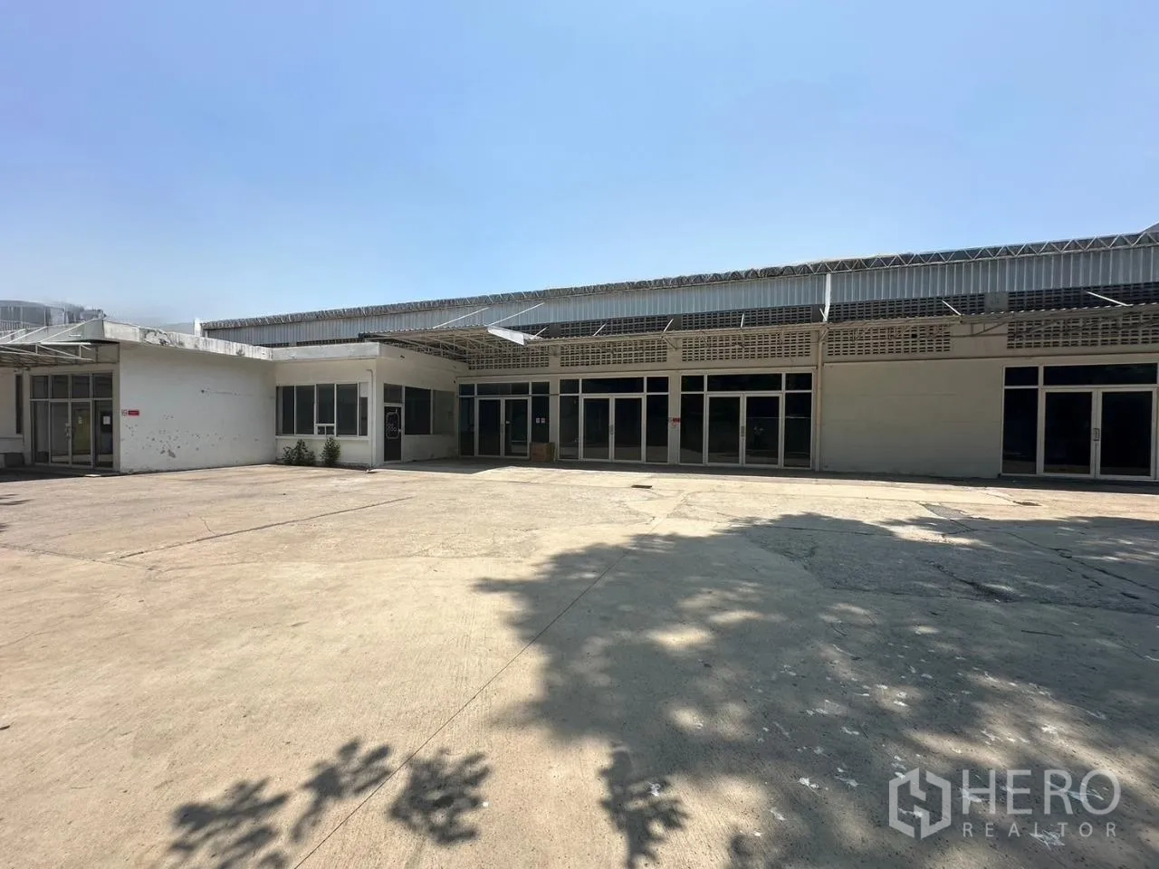 Warehouse for rent in Din Daeng, Bangkok - Single-story warehouse exterior with a wide concrete yard and glass-front entrances under a metal awning.