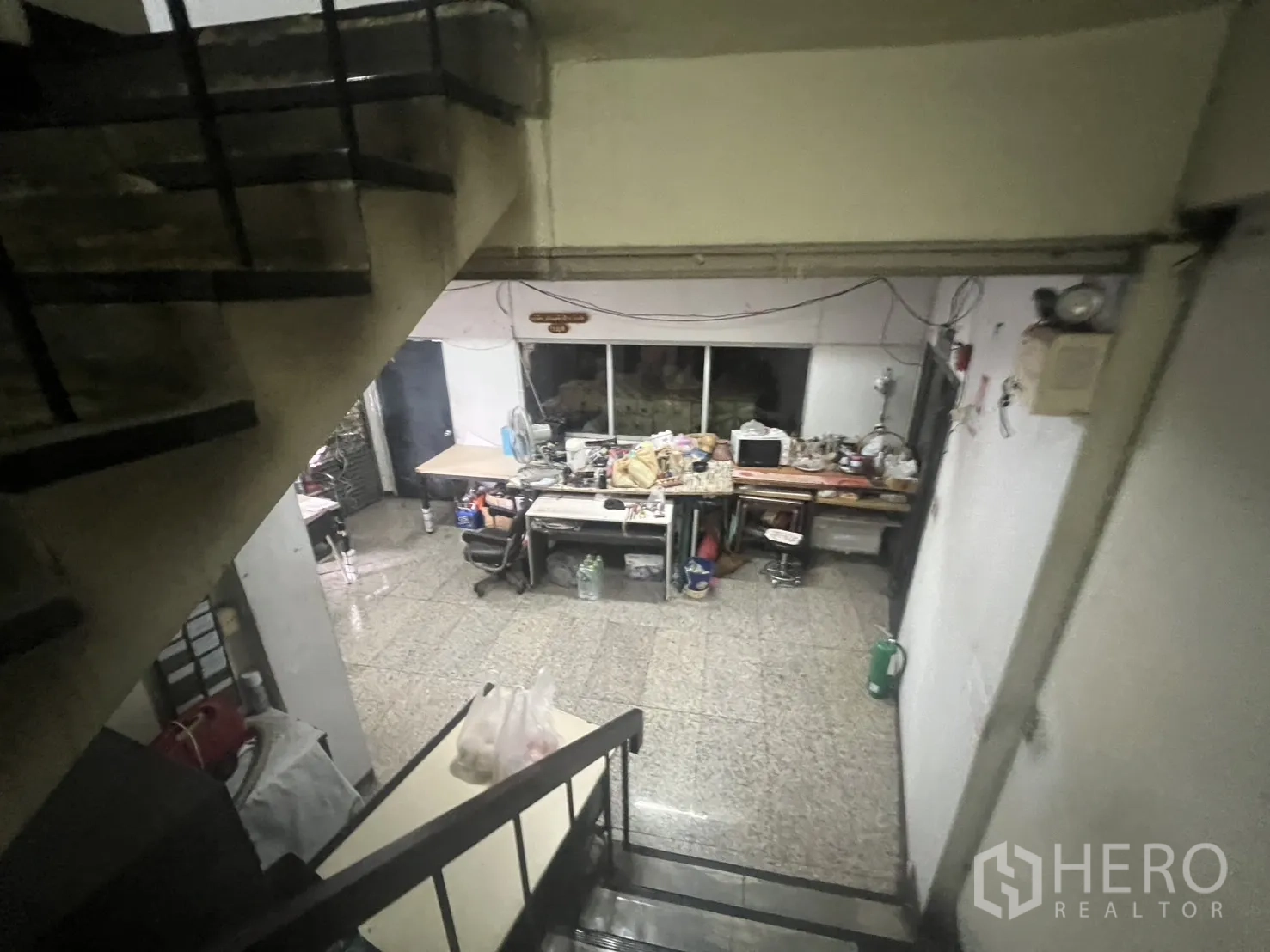 อาคารพาณิชย์ ให้เช่า - มุมมองจากบันไดลงไปยังพื้นที่ออฟฟิศชั้นล่างและโต๊ะทำงาน.